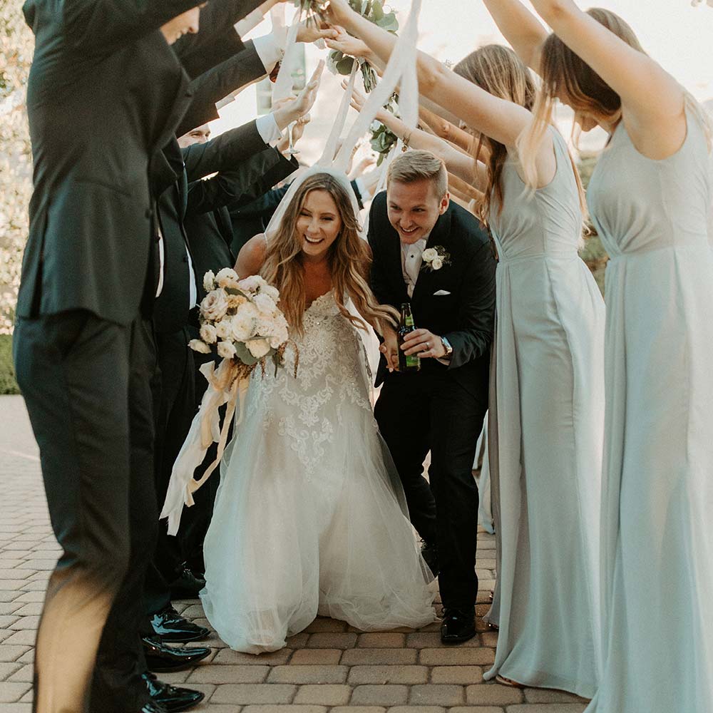 A bride and groom smiling and bent over as they go through a canopy of raised arms of their bridesmaids and groomsman at this outdoor winery wedding in Sacramento.