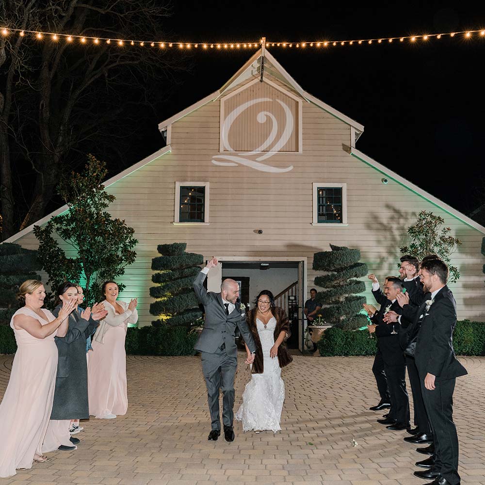 The bride and groom are introduced as a couple as they giddily walk past their wedding party toward the guests with the backdrop of a 1920's barn.