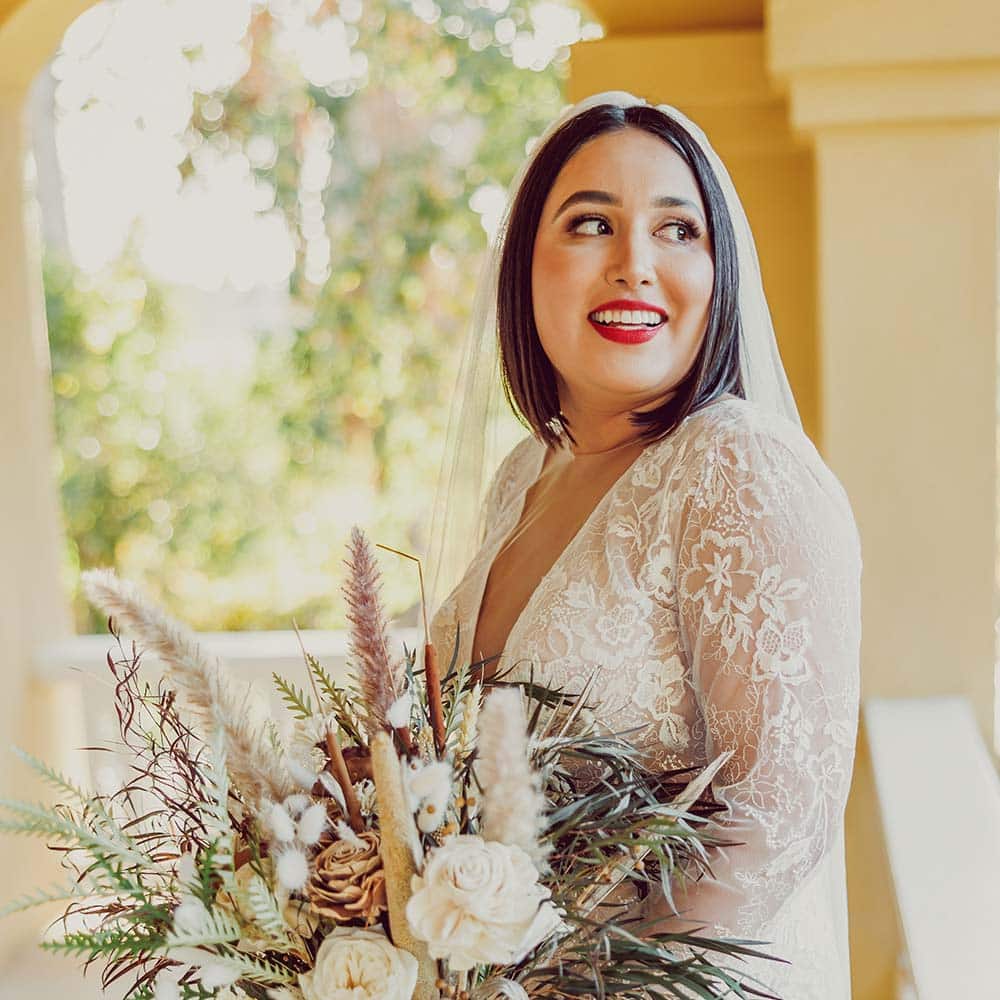 The bride sits holding her bouquet on the balcony of a 1920's craftsman home eagerly looking in the distance and dreaming about her day at her winery wedding in Sacramento.