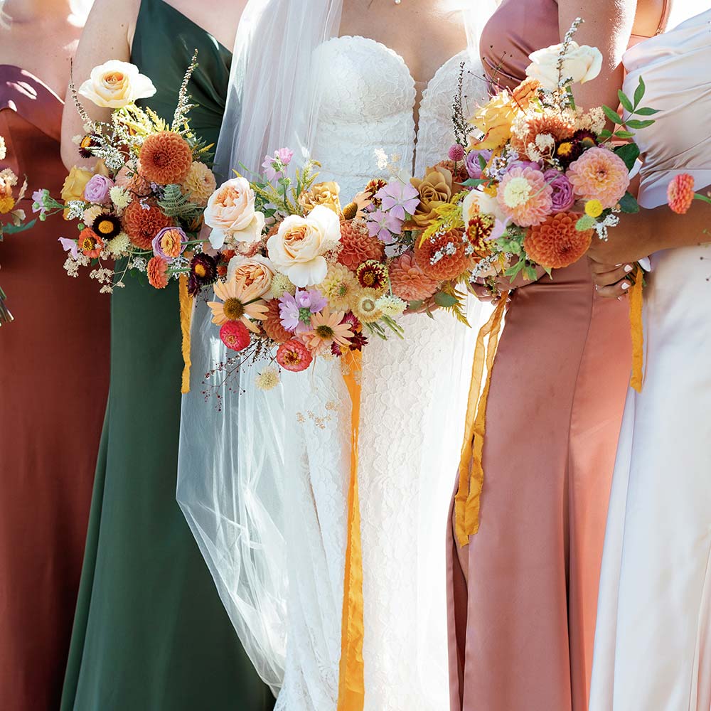 The bride and 4 of her bridesmaids in rust, green and orange dresses with just their bright bouquets and dresses showing at this outdoor winery wedding in Sacramento.