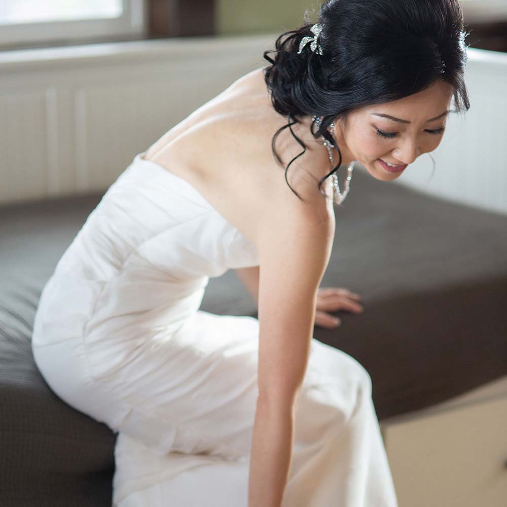 A bride all in white with a big smile on her face as she is putting her beige shoe on while getting ready for her outdoor winery wedding.