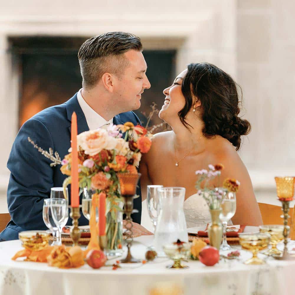 A close up of the bride and groom smiling at each other at their head table and in front of the outdoor fireplace at their outdoor winery wedding in Sacramento.