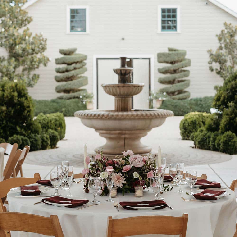 A view of the 1918 barn in full view of a fountain as a backdrop to the winery wedding place setting at a guests table in Sacramento.