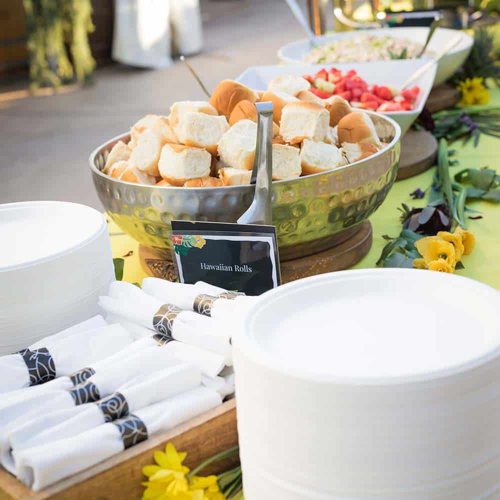 A buffet table in yellow linens with plates, napkins and trays of food.