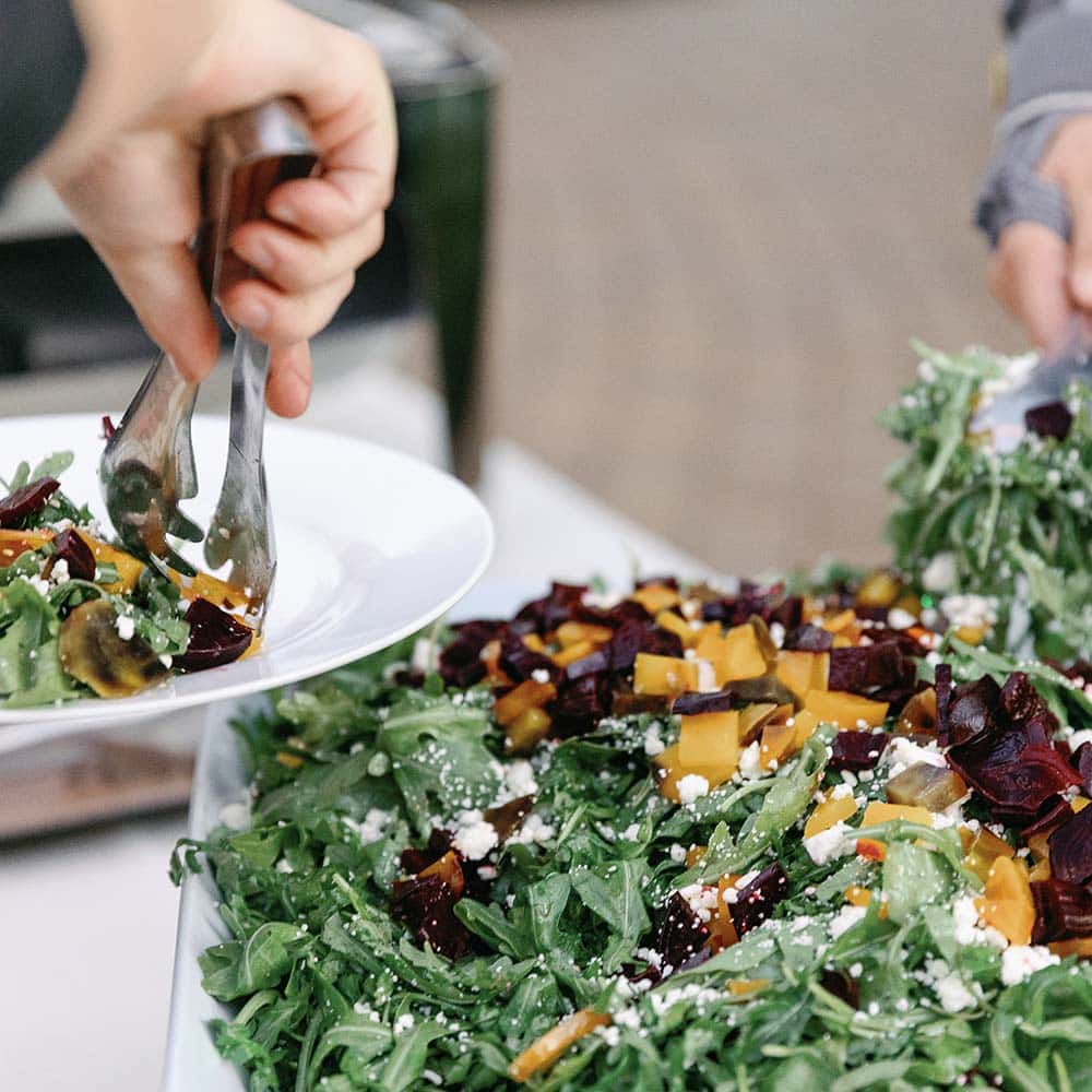 Guests go through a buffet line and dish up salad on their plates at their corporate event.