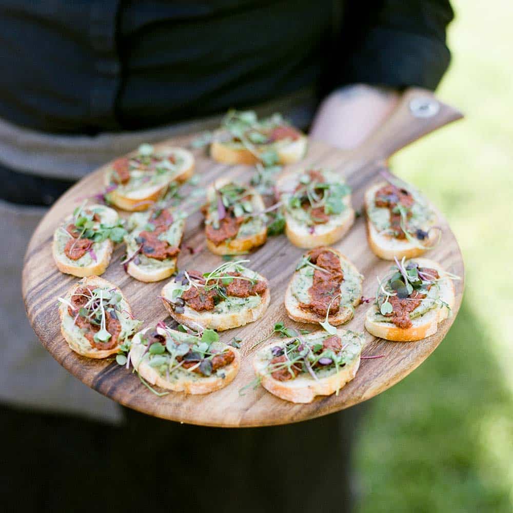 A server hold a tray of appetizers on a wooden board.